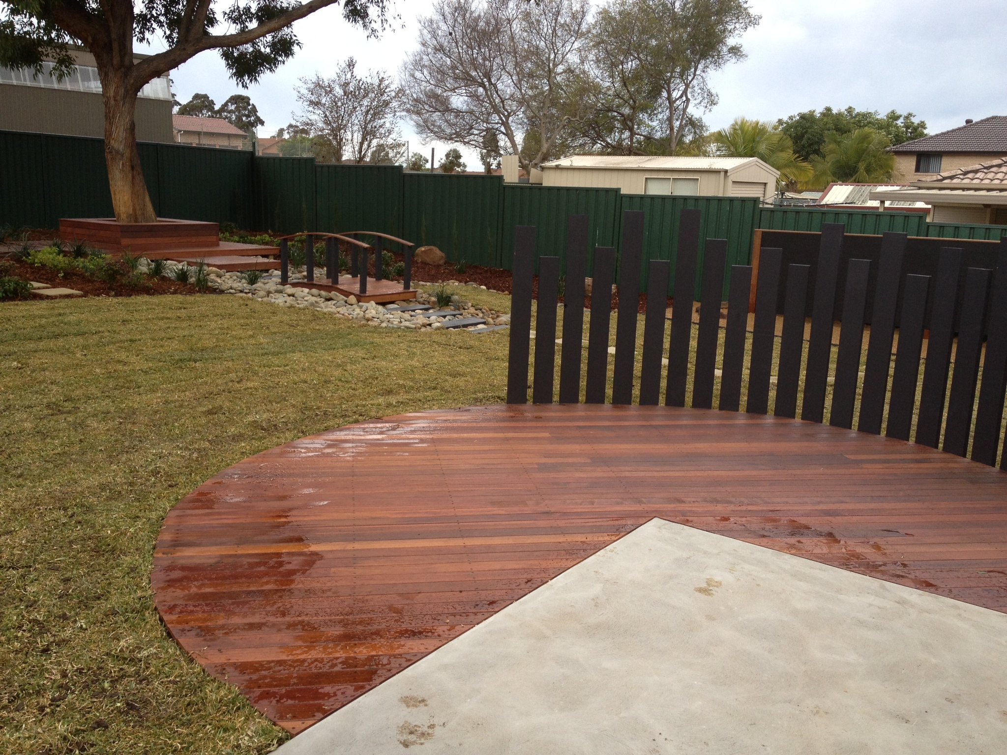 Curved timber deck meeting concrete patio with a feature timber-batten privacy screen.