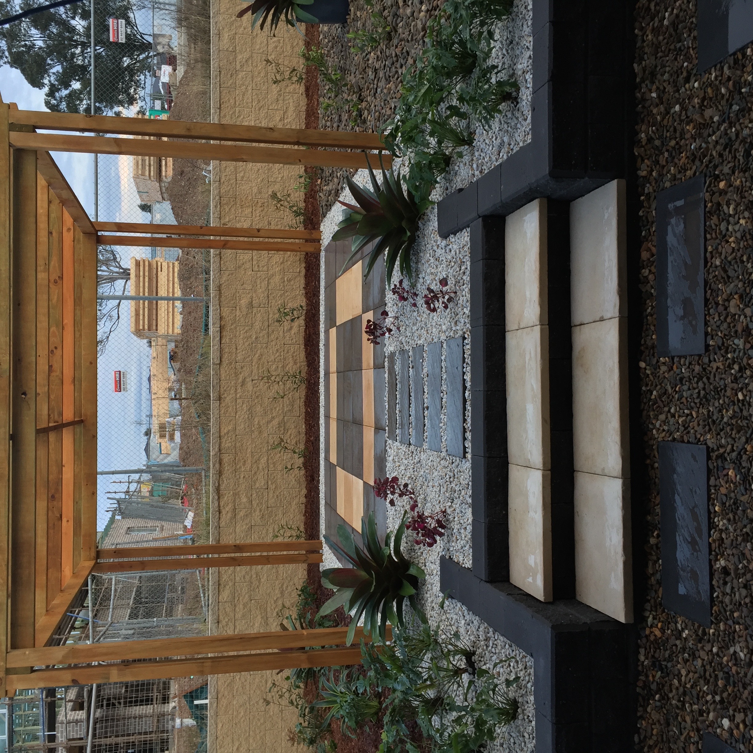 Timber pergola over sandstone-and-bluestone paving with raised garden beds either side.