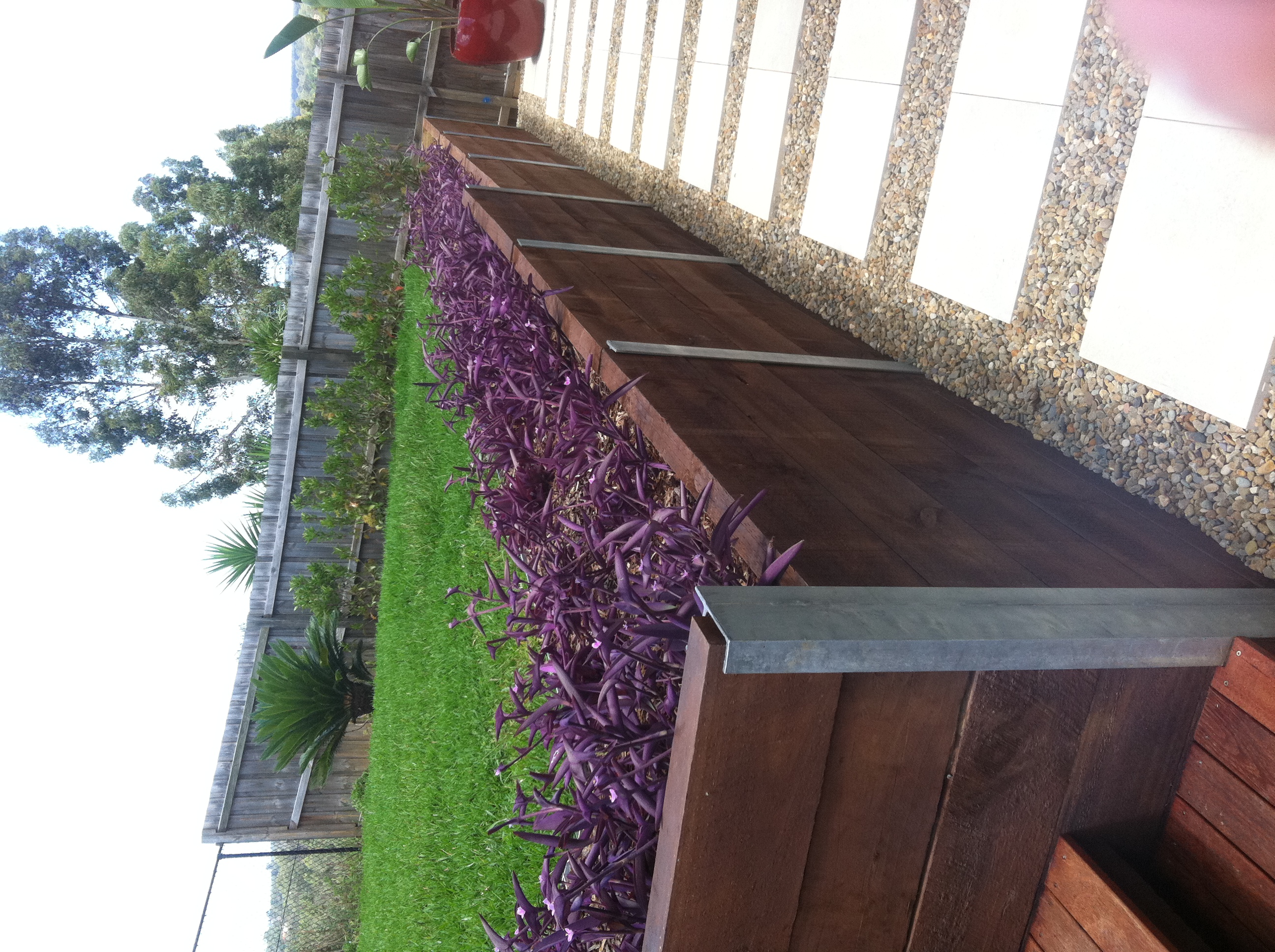 Long timber sleeper retaining wall doubling as a feature planter behind a paver-and-pebble path.