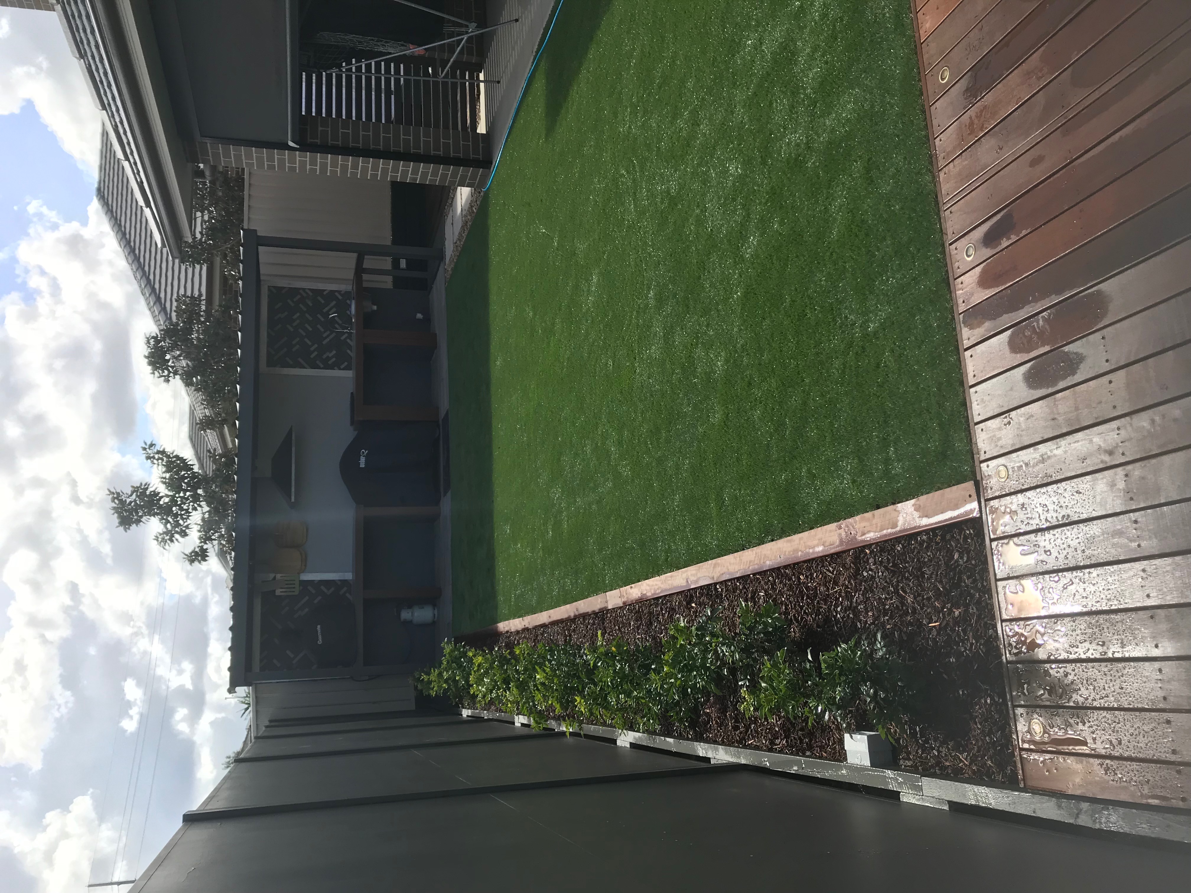 Synthetic turf courtyard with mulched garden strip, hardwood deck and outdoor kitchen pergola.